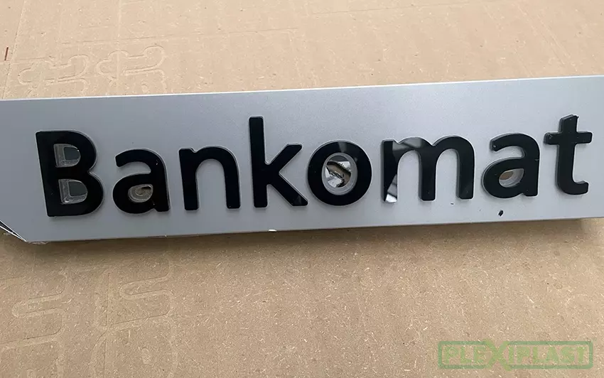 Reklamní světelný nápis 'Bankomat' vytvořený soulepem čirého a černého plexiskla